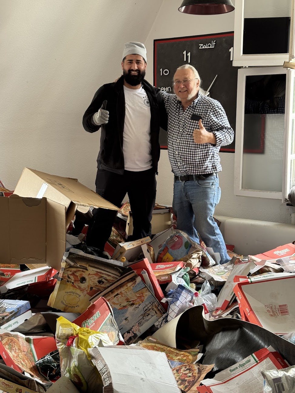 Mitarbeiter von Robins mit Daumen hoch in einer Wohnung voller Pizzakartons – mitten im Einsatz