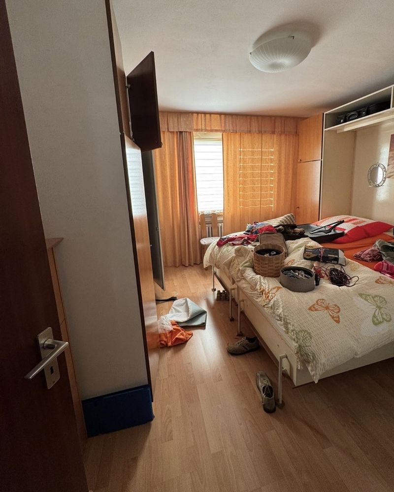 Vorher: Schlafzimmer mit Bett, Schränken und Kleidung