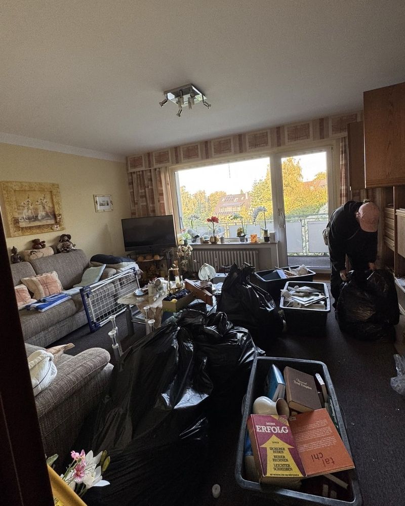Vorher: Wohnzimmer mit Sofas, Schrankwand, Kisten und Müllsäcken
